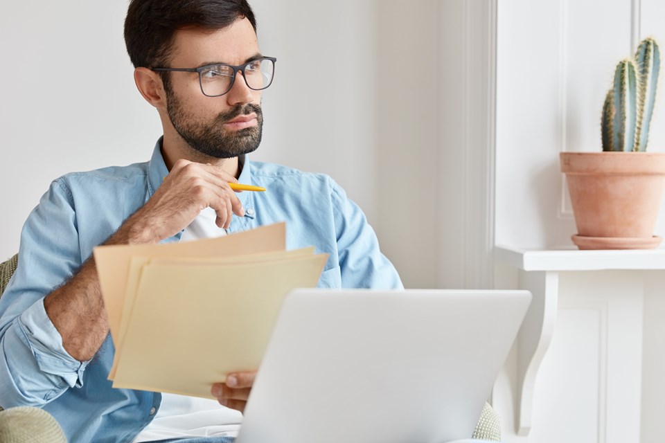 bearded-pensive-man-works-from-home-counts-financial-data-holds-paper-documents