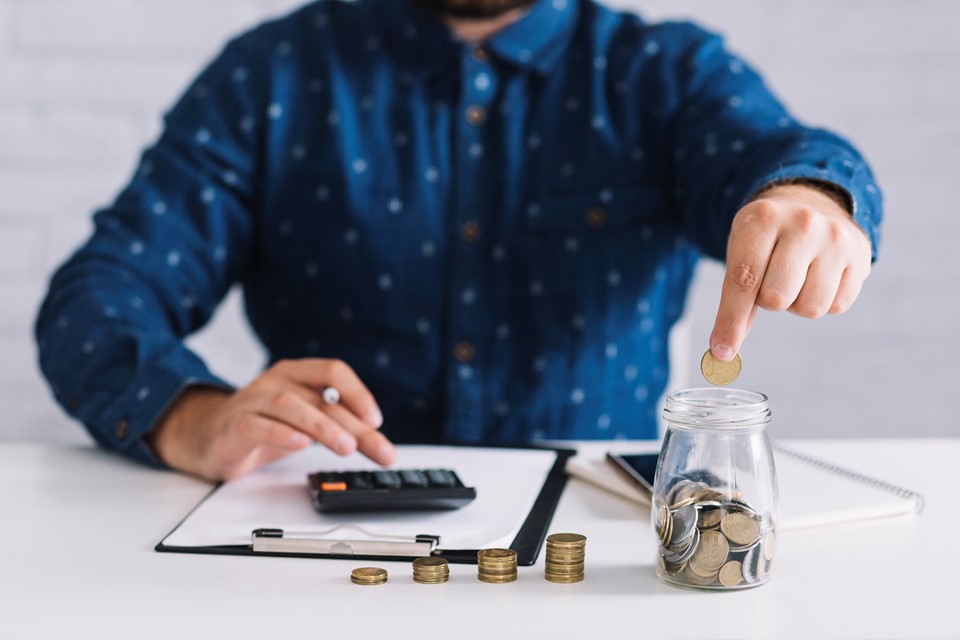 businessman-putting-coins-jar-using-calculator-workplace
