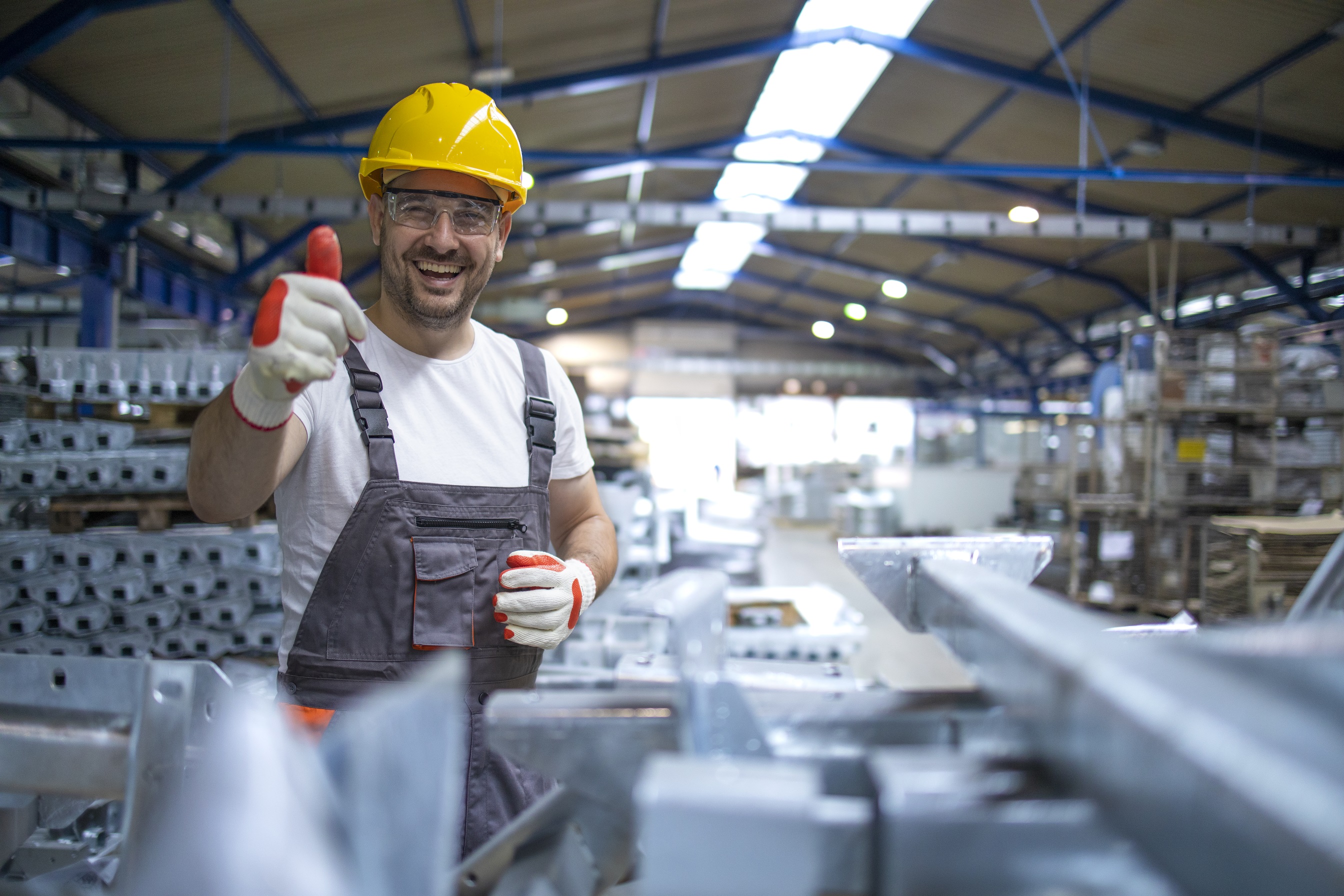 portrait-of-factory-worker-in-protective-equipment-holding-thumbs-up-in-production-hall
