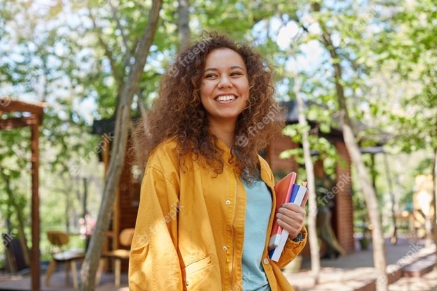 retrato-de-sorridente-jovem-estudante-encaracolado-de-pele-escura-linda-no-terraco-de-um-cafe-segurando-livros-didaticos-vestindo-casaco-amarelo-aproveita-o-dia_295783-2562-1